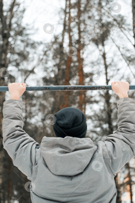 Скачать Мужчина в одежде выполняет упражнение на турнике на улице зимой. Спортивное оборудование для тренировок на открытом воздухе фотосток Ozero