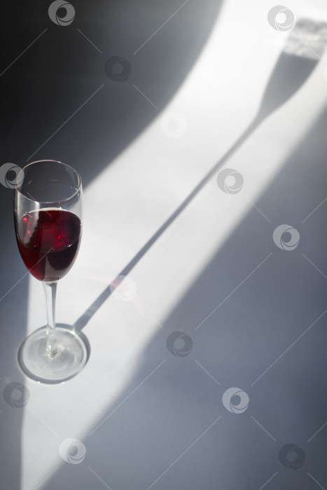 Скачать Бокал красного вина и тень на белом фоне в солнечный день. Минималистичная фотография натюрморта фотосток Ozero