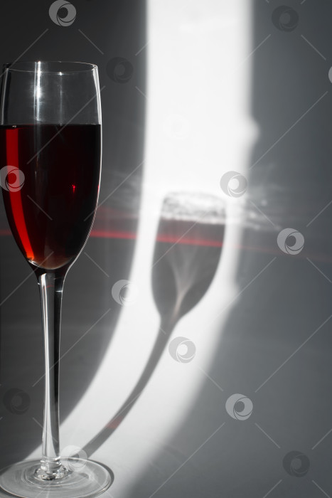 Скачать Солнечный свет, пробивающийся сквозь бокал красного вина. Тень и отражения от напитка на светлом фоне, вертикальная фотография фотосток Ozero