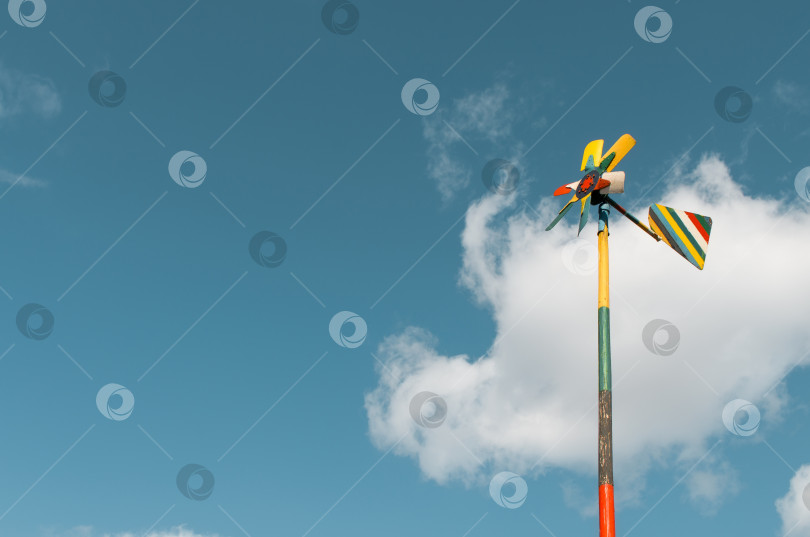 Скачать Самодельный разноцветный деревянный флюгер на шесте на фоне голубого облачного неба. Скопируйте место для текста. фотосток Ozero