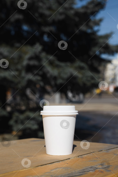 Скачать Одноразовый стаканчик с кофе стоит на столике на улице в городе. Пустой белый картонный стаканчик. Вертикальная фотография фотосток Ozero