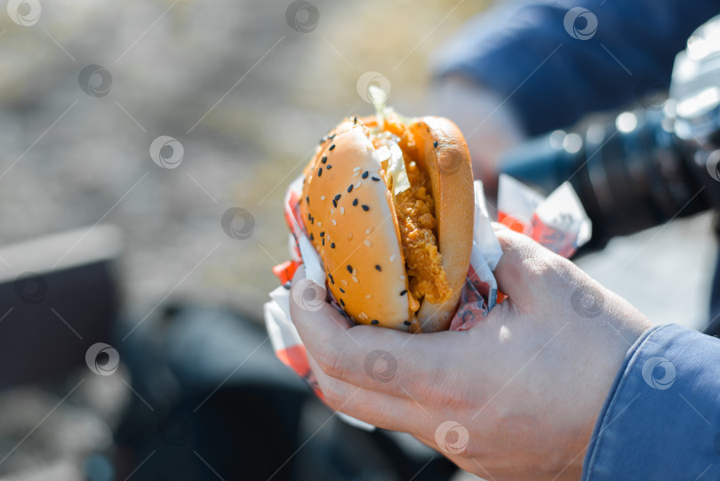 Скачать Мужчина ест бургер на улице в солнечный день. Крупный план мужской руки, держащей фастфуд, выборочный фокус фотосток Ozero
