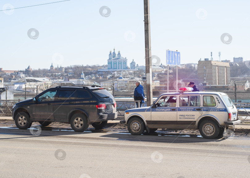 Скачать Полицейский патрульный внедорожник с мигающими синими и красными огнями остановил автомобиль за нарушение правил дорожного движения, и они стоят на обочине дороги на фоне городского пейзажа. Смоленск, Россия 04.12.2021 фотосток Ozero