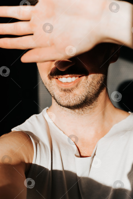 Скачать Портрет улыбающегося мужчины с бородой, закрывающего лицо от яркого солнца, в помещении. Концепция жаркий солнечный день, закат, восход солнца фотосток Ozero