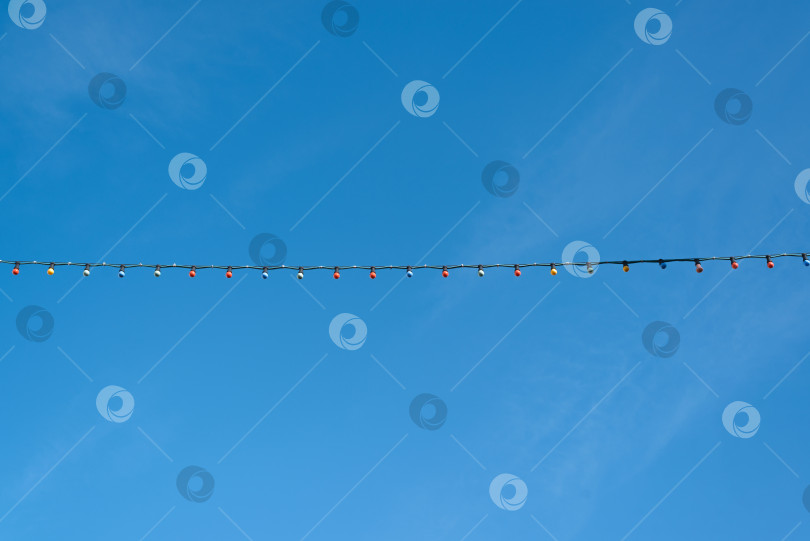 Скачать Уличная гирлянда с разноцветными лампочками на фоне ясного голубого неба в солнечный день. Пространство для копирования фотосток Ozero