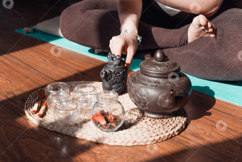 Скачать Чайная церемония в помещении утром. Женщина в позе лотоса, держащая маленький чайник, крупным планом фотосток Ozero