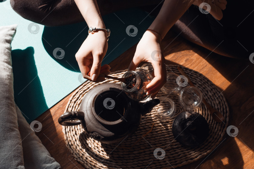 Скачать Женщина готовит травяной чай в помещении на рассвете. Женские руки заваривают горячий напиток в глиняном чайнике крупным планом. Концепция чайной церемонии, релаксации фотосток Ozero