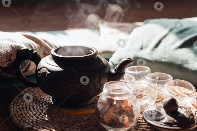 Скачать Горячий чай в глиняном чайнике, поднимающийся пар, кружки на подносе внутри комнаты. Концепция утренней чайной церемонии. Крупный план, выборочный фокус фотосток Ozero