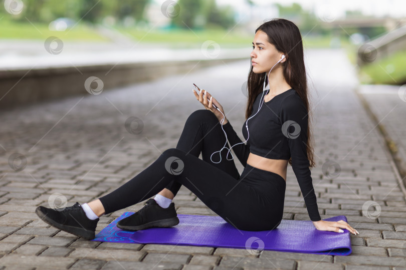 Скачать Молодая спортивная брюнетка в спортивной одежде слушает музыку, сидит фотосток Ozero