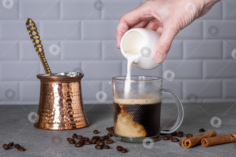 Скачать Женская рука наливает сливки в стеклянную чашку с кофе фотосток Ozero