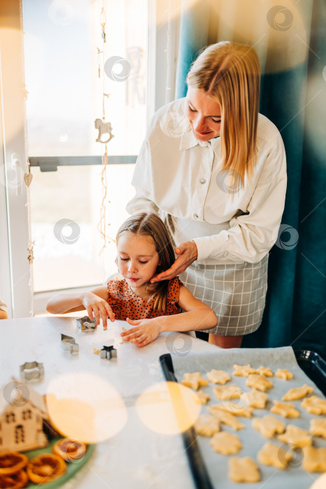 Скачать Счастливые мать и дочь готовят на кухне, дочь смеется и наслаждается семейным приготовлением домашнего печенья. Солнечный день дома в закрытом помещении фотосток Ozero