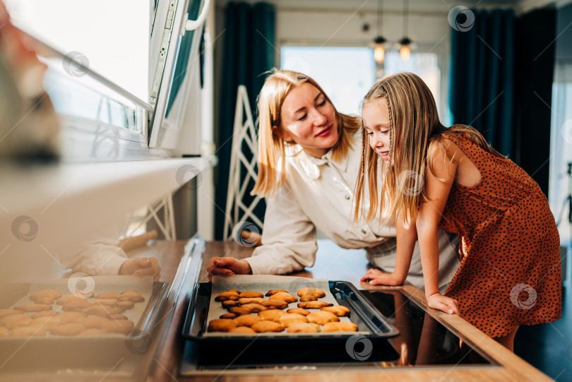 Скачать Счастливые мать и дочь готовят на кухне, дочь смеется и наслаждается семейным приготовлением домашнего печенья. Солнечный день дома фотосток Ozero