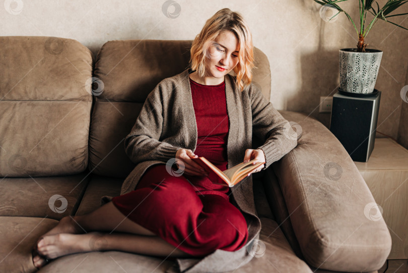 Скачать Задумчивая девушка-студентка читает книгу. Молодая женщина учится дома, сидя на бежевом диване фотосток Ozero