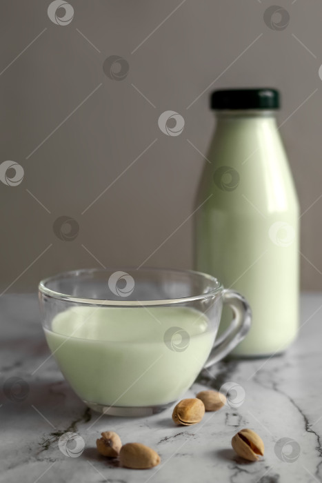 Скачать Фисташковое молоко в чашке рядом с бутылкой молока и фисташками. фотосток Ozero
