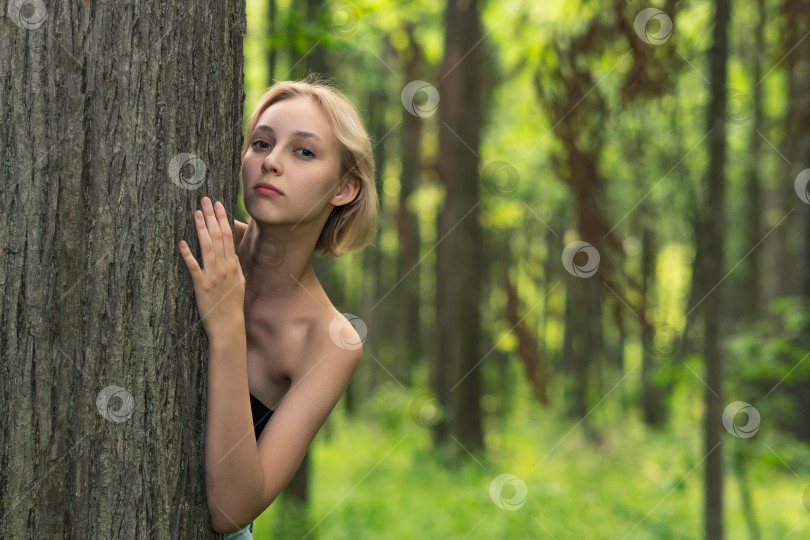 Скачать красивая девушка выглядывает из-за дерева в лесу фотосток Ozero