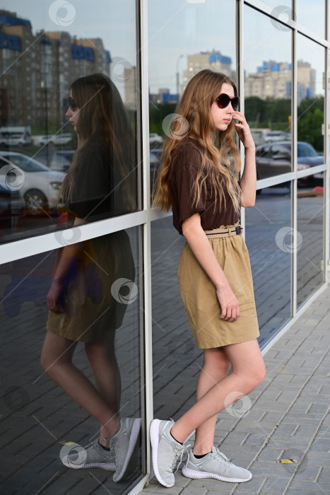Скачать Девочка-подросток в солнцезащитных очках смотрит на свое отражение в стекле фотосток Ozero