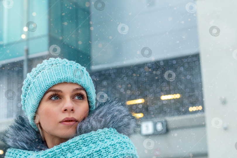 Скачать Молодая женщина в шапке и шарфе в заснеженном городе зимой. С надеждой смотрит в будущее. Крупный план фотосток Ozero
