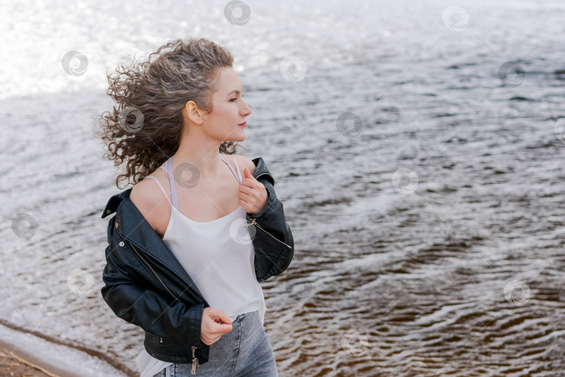 Скачать Молодая стильная женщина в светлой футболке и кожаной куртке с вьющимися волосами фотосток Ozero