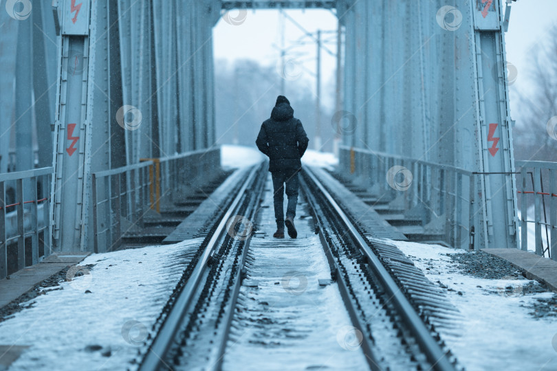 Скачать Одинокий мужчина в черной одежде прогуливается зимой по железнодорожному полотну фотосток Ozero