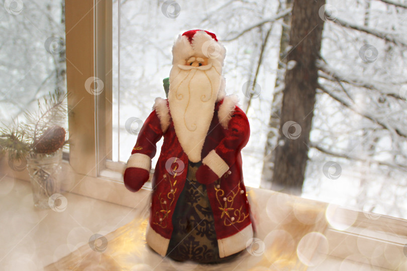 Скачать Дед Мороз в красной шубе на подоконнике на фоне зимнего снежного пейзажа в открытое окно прилетел поздравить с Новым годом и Рождеством праздничным вечером. Сказка, тайна. фотосток Ozero