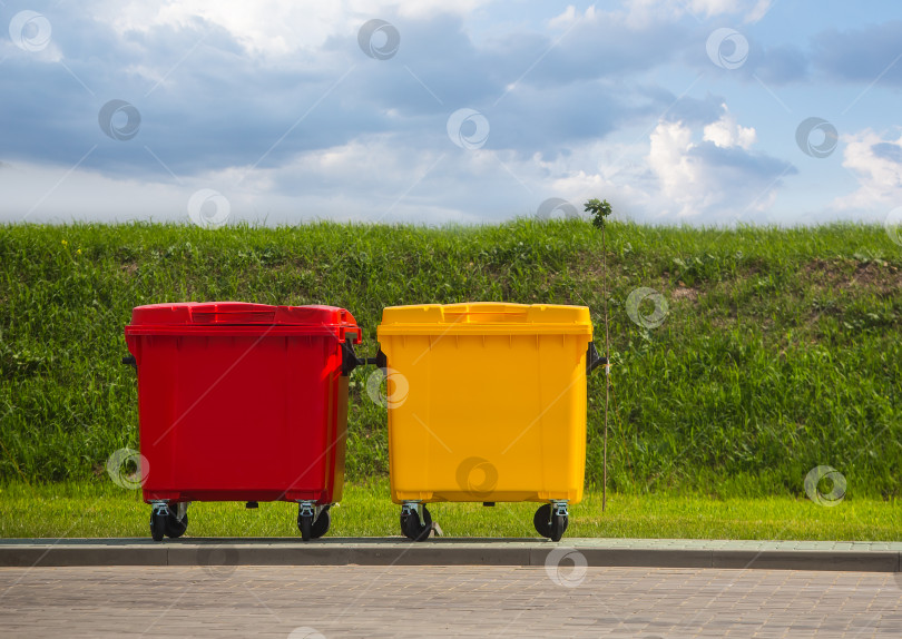 Скачать Пластиковые контейнеры для мусора красные и желтые на улице на газоне фотосток Ozero