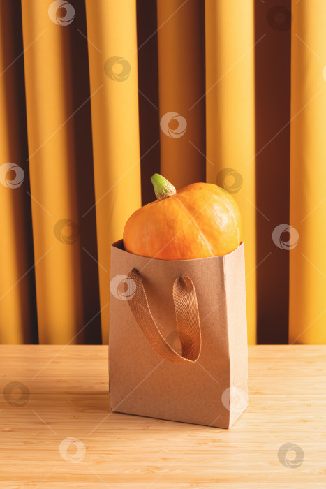 Скачать Осенняя композиция с оранжевой тыквой в крафт пакете на фоне желтых штор. фотосток Ozero