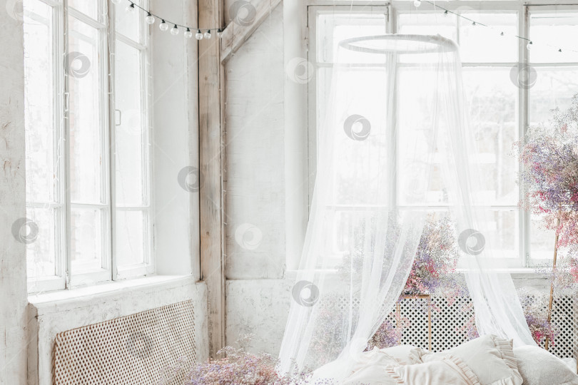 Скачать Кровать в светлой спальне в пастельных тонах в стиле бохо, трендовом цвете 2023 года. Комната украшена сиреневыми и розовыми цветами гипсофилы, винтажный декор в комнате в стиле ретро лофт фотосток Ozero