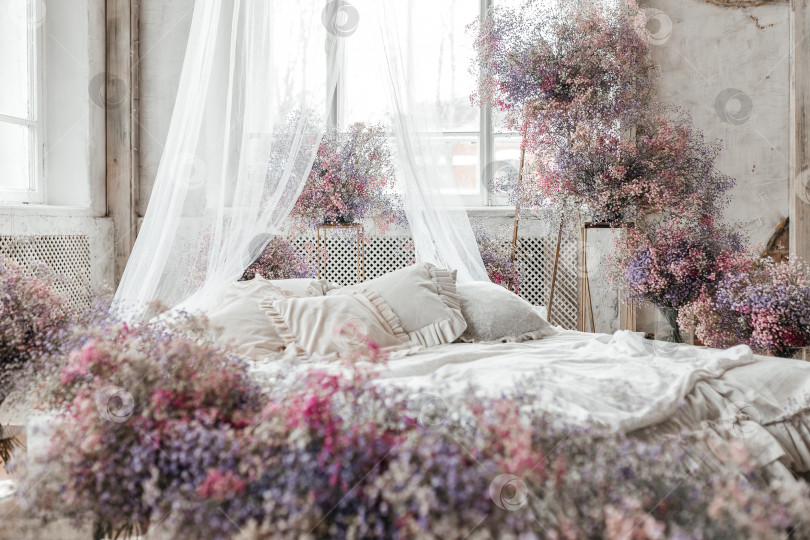 Скачать Кровать в светлой спальне в пастельных тонах в стиле бохо, трендовый цвет 2023 года. Комната украшена сиреневыми и розовыми цветами гипсофилы, винтажный декор в комнате в стиле ретро лофт фотосток Ozero