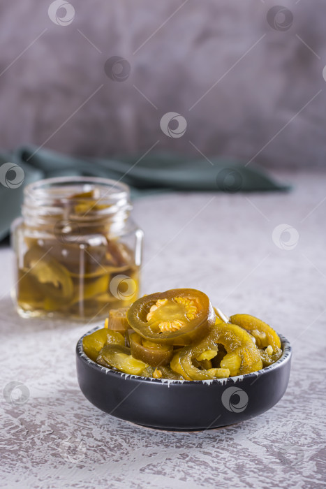 Скачать Нарезанный маринованный перец халапеньо в миске и стеклянной банке на столе v фотосток Ozero