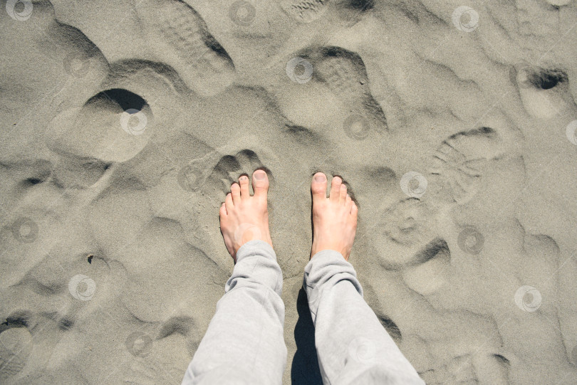 Скачать Мужские босые ноги на песке среди следов обуви. Концепция фотосток Ozero
