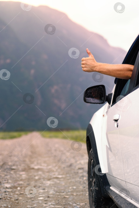 Скачать Рука мужчины показывает поднятый большой палец из своей машины. Летняя поездка на автомобиле фотосток Ozero