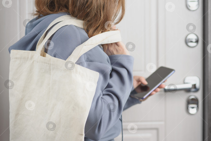 Скачать Женщина с эко-сумкой просматривает список покупок на своем телефоне. фотосток Ozero