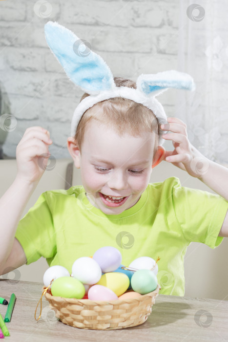 Скачать Пасхальные дети. Счастливый мальчик с кроличьими ушками на голове играет дома с крашеными яйцами. Готовимся к Пасхальной охоте за большими яйцами. Пасхальный кролик. Пасхальные яйца. Вертикальная фотография фотосток Ozero