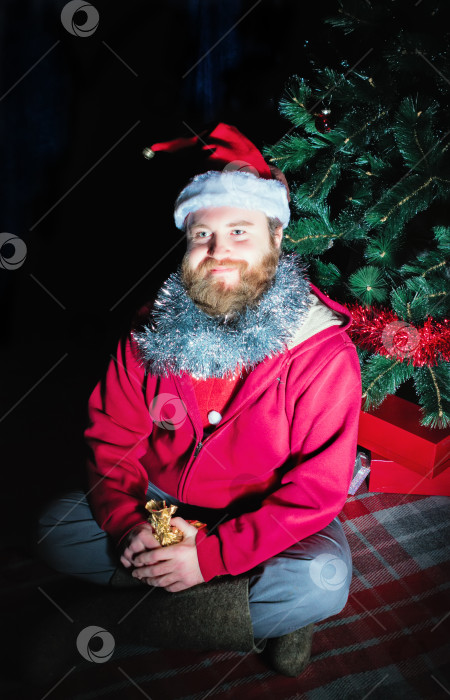Скачать Мужчина в костюме Санты Сидит под Рождественской елкой фотосток Ozero