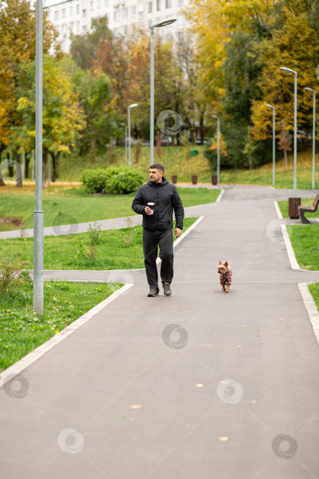 Скачать Мужчина гуляет по парку с собакой и чашкой кофе фотосток Ozero