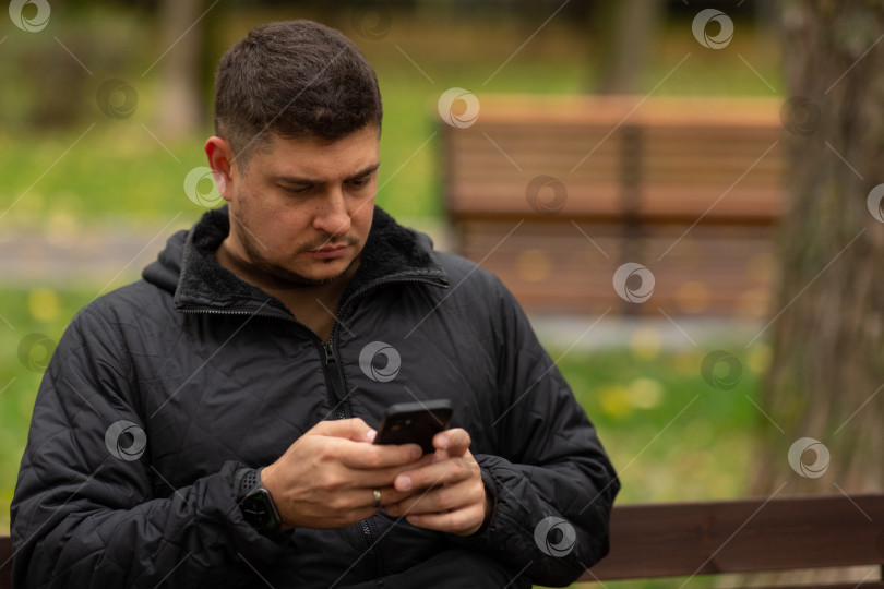 Скачать Мужчина сидит осенью на скамейке в парке и что-то печатает фотосток Ozero