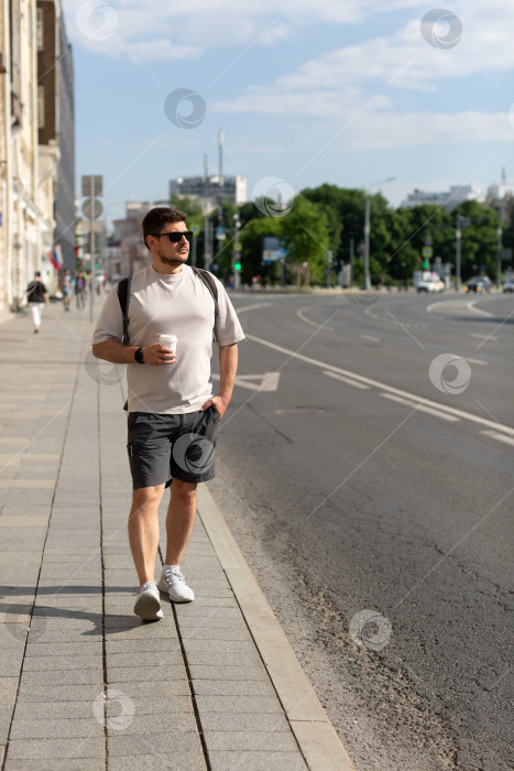 Скачать Мужчина идет по городской улице с чашкой кофе фотосток Ozero