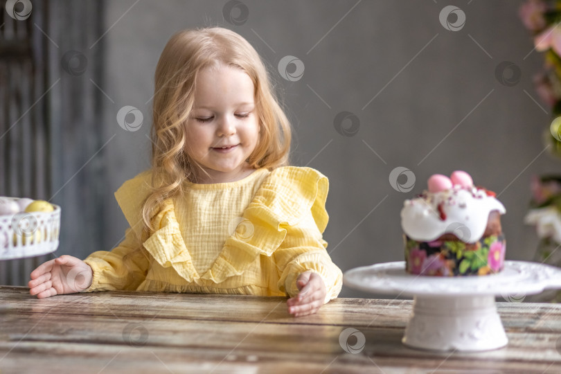 Скачать Маленькая светловолосая девочка в желтом платье сидит за праздничным пасхальным столом с кроликами.Младенец и кролик. Концепция Пасхи.Пасха за столом. Христианская традиция. фотосток Ozero