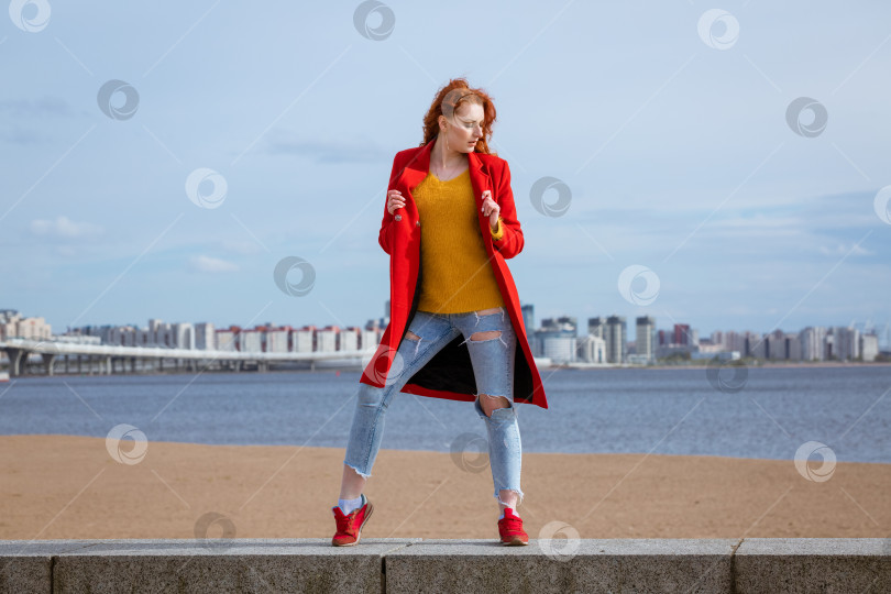 Скачать Рыжеволосая женщина позирует на фоне реки в городе со зданиями на заднем плане. фотосток Ozero