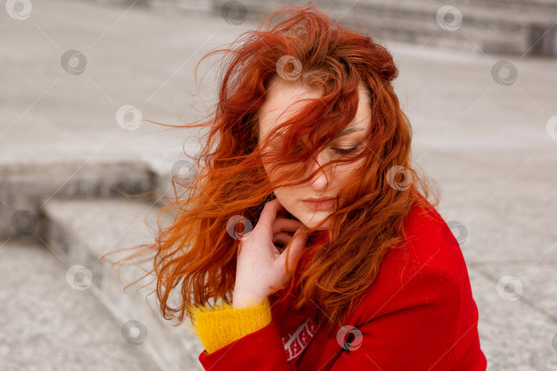 Скачать портрет женщины в красном пальто на улице, ее волосы падают на лицо. фотосток Ozero