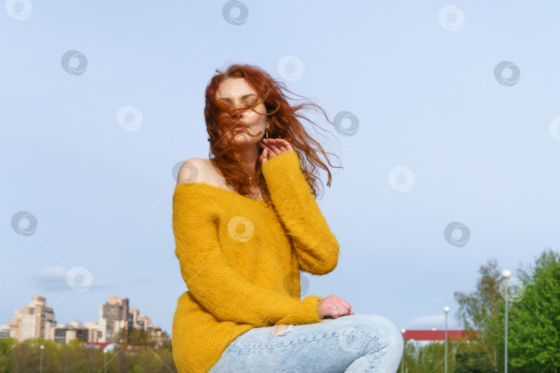 Скачать Великолепная счастливая рыжеволосая женщина сидит на битоне и траве, отдыхая в местном парке фотосток Ozero