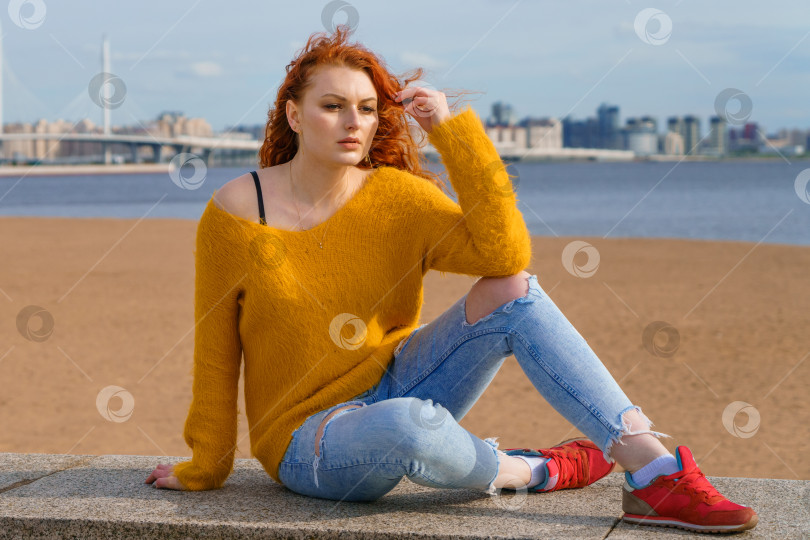 Скачать Молодая рыжеволосая девушка в желтом свитере и джинсах. Симпатичная женщина сидит фотосток Ozero