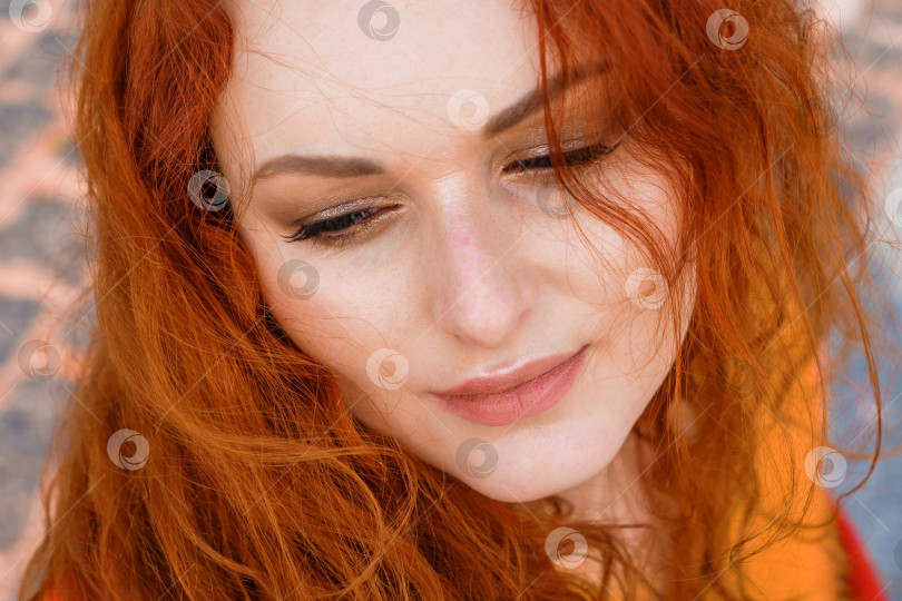 Скачать Портрет крупным планом молодой кавказской женщины с рыжими вьющимися волосами в красном пальто на ветру фотосток Ozero