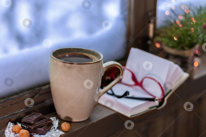 Скачать Зимний уютный натюрморт с чашкой кофе, книгой, бокалами и рождественской елкой. Сугробы за окном. Хюгге фотосток Ozero