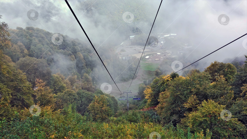 Скачать Туманный осенний день в горах Кавказа. Канатная дорога проходит над лесом фотосток Ozero