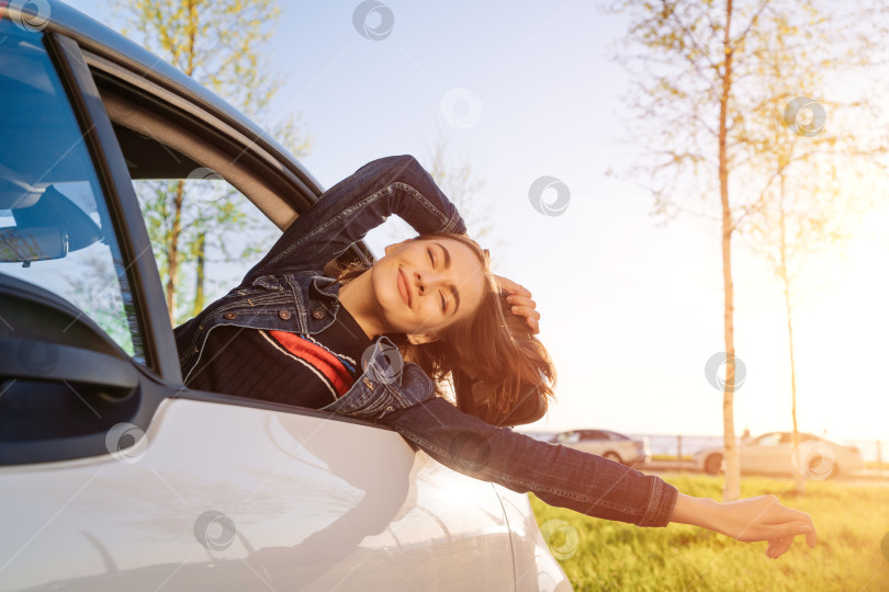 Скачать Счастливая женщина машет рукой из машины с открытым окном на фоне голубого неба и солнца. фотосток Ozero