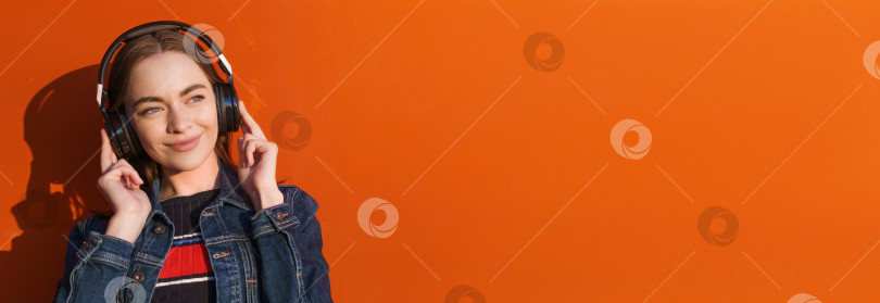 Скачать Портрет счастливой улыбающейся молодой женщины в наушниках, слушающей музыку на оранжевом фотосток Ozero
