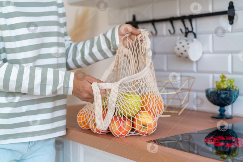 Скачать Анонимная женщина покупает продукты в эко-сумке. Сортировка яблок на кухне. Концепция покупок с нулевыми отходами фотосток Ozero