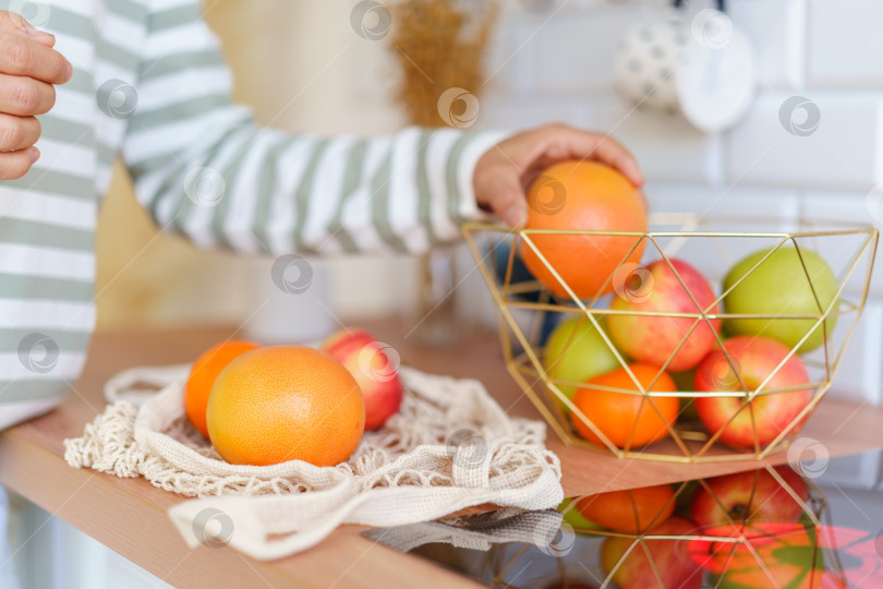 Скачать Безликий человек хватает спелое яблоко из вазы с фруктами на кухонном столе. Сортировка после продуктового магазина фотосток Ozero