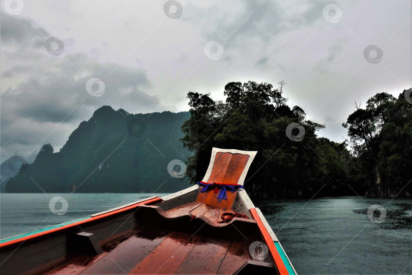 Скачать Яркая деревянная лодка плывет по озеру, на воде появляются круги от капель дождя. фотосток Ozero